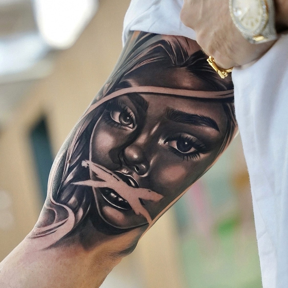Black and grey realism inner bicep tattoo of a woman's face with brushstroke overlay