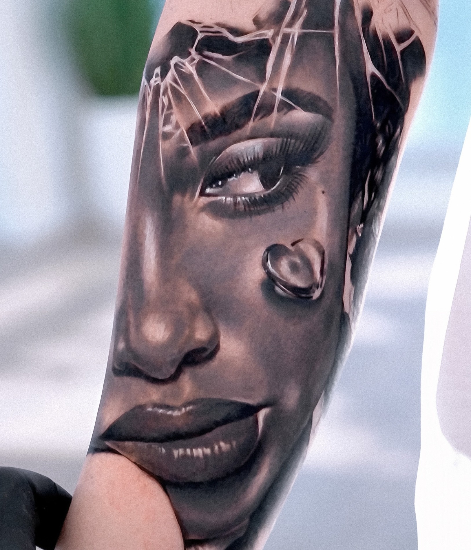Black and grey forearm portrait of a woman with shattered glass overlay and heart-shaped droplet